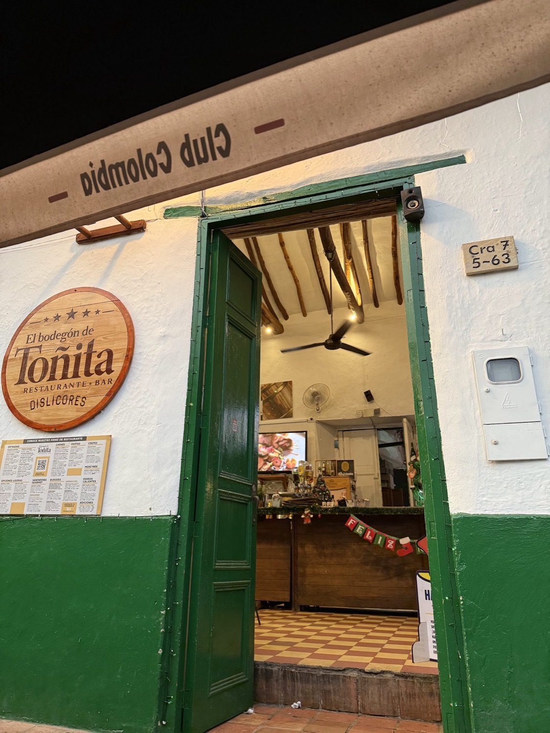 Fachada del Bodegón de Toñita: pared blanca, puerta verde y su letrero de madera