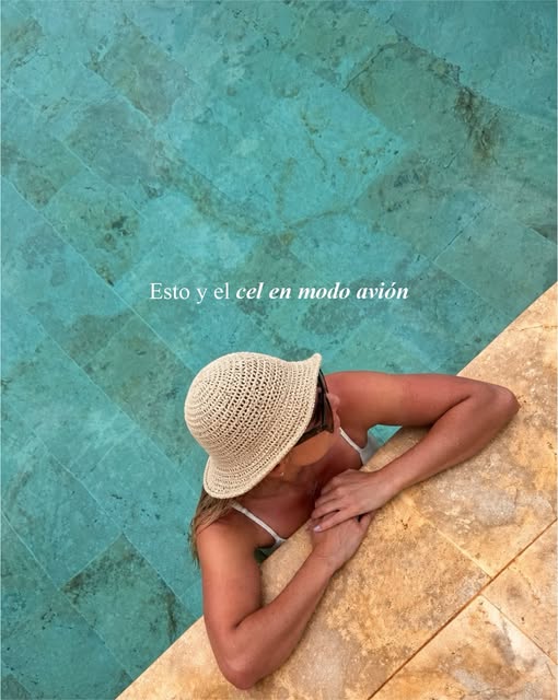 Huésped apoyada en el borde de la piscina con sombrero