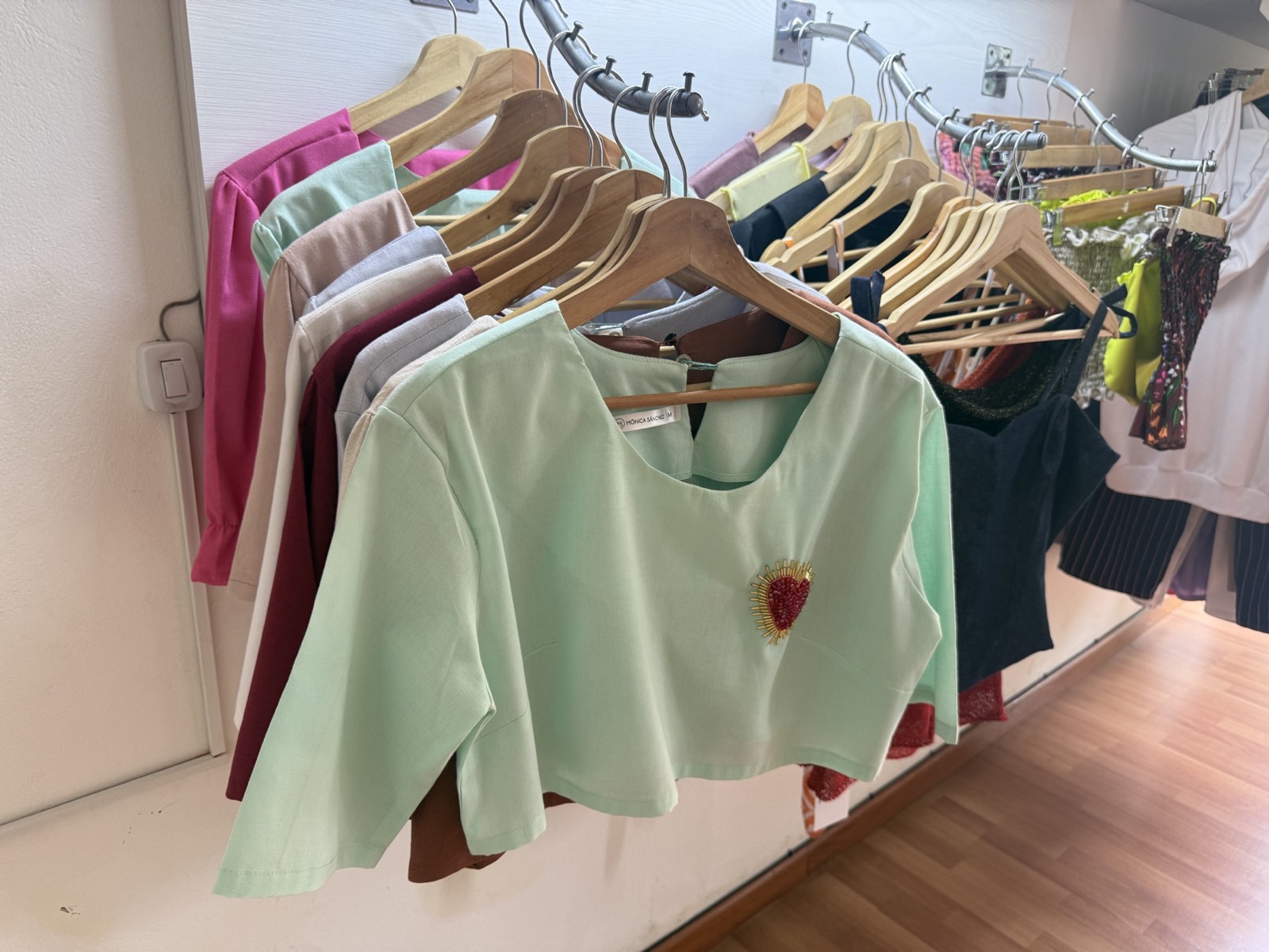 Blusas en tonos pastel colgadas en ganchos de madera