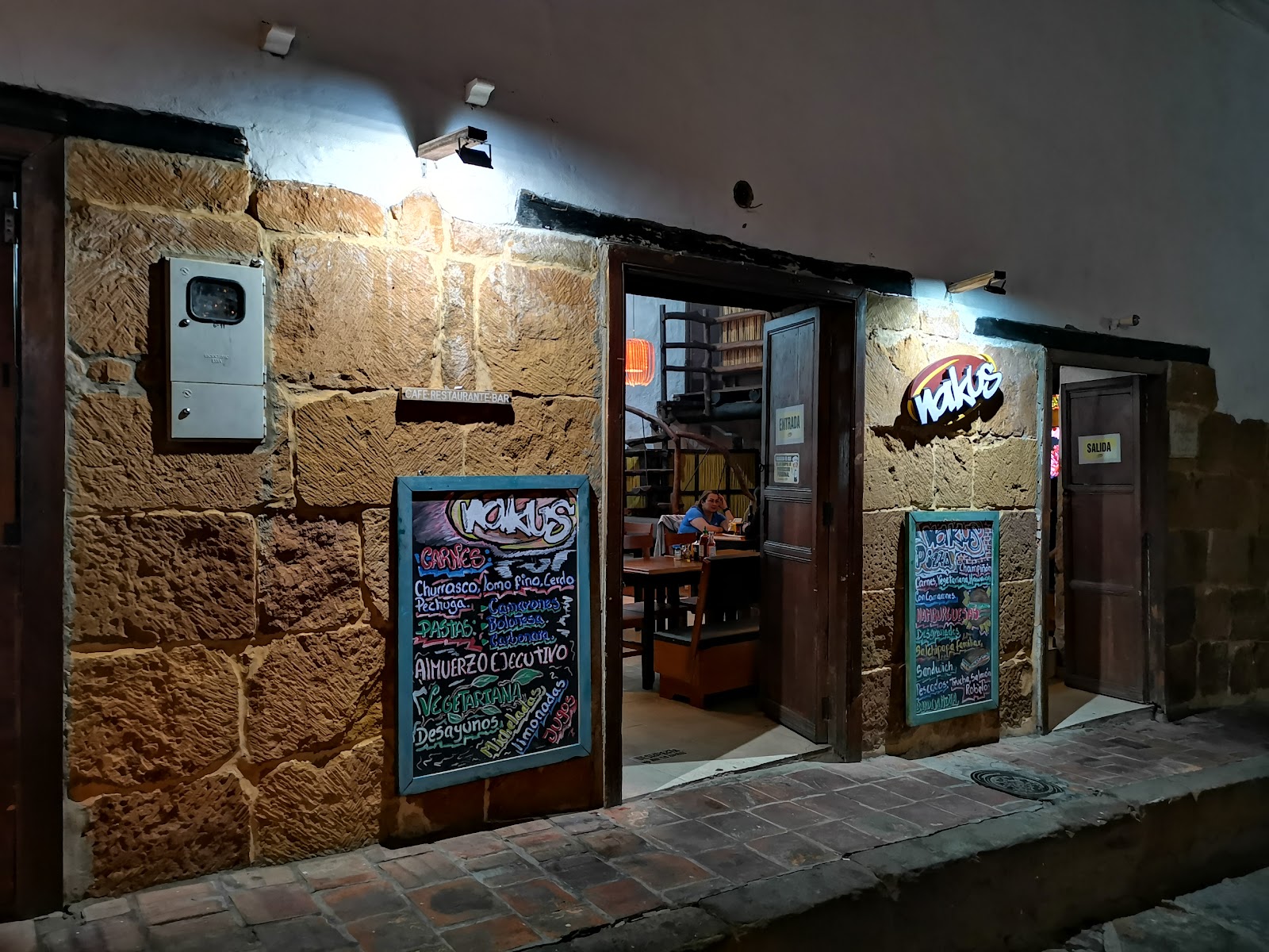 Fachada de piedra de Nakus de noche, con pizarras de la carta en la entrada
