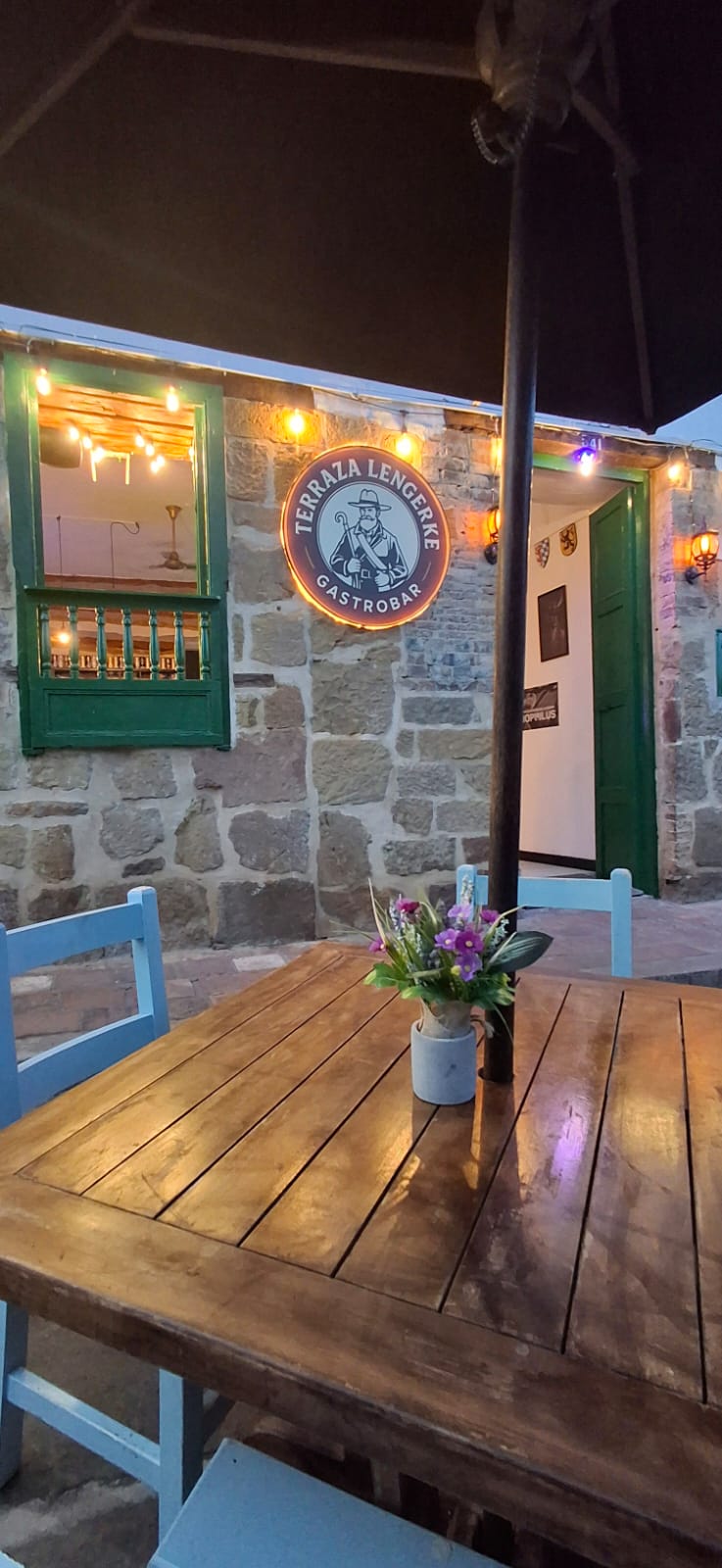 Mesa de madera con flores frente a la fachada de piedra del gastrobar
